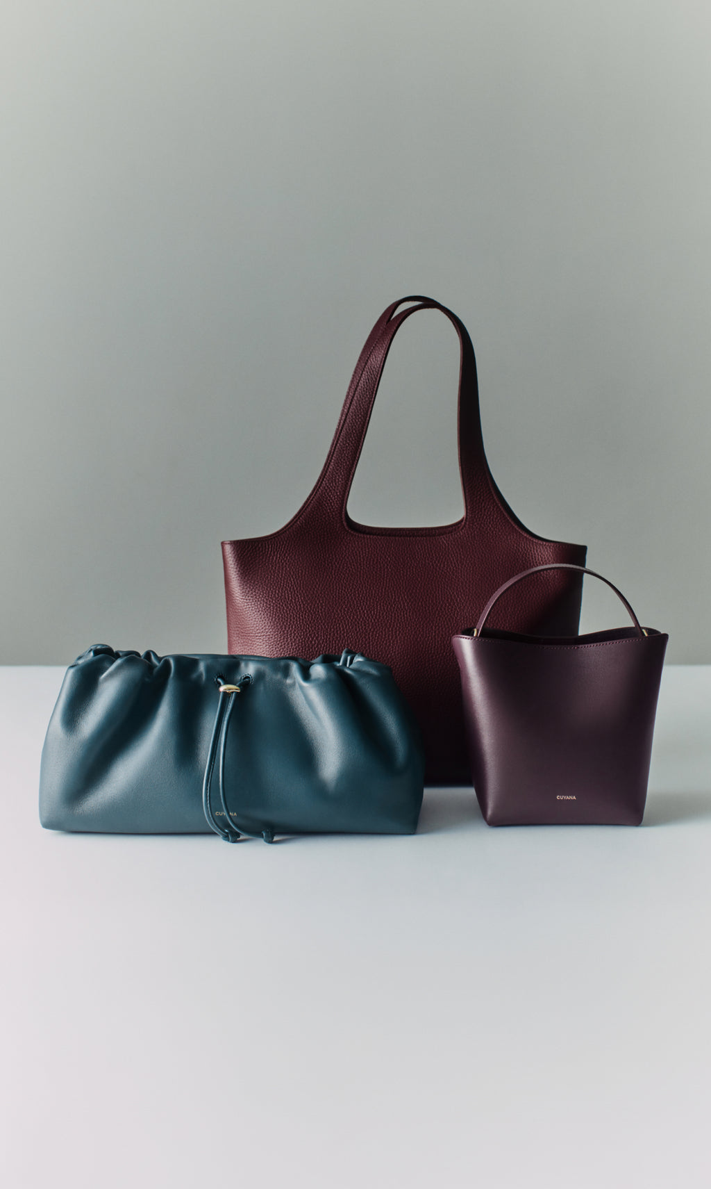 Three handbags displayed on a surface, includes tote, clutch and crossbody styles.