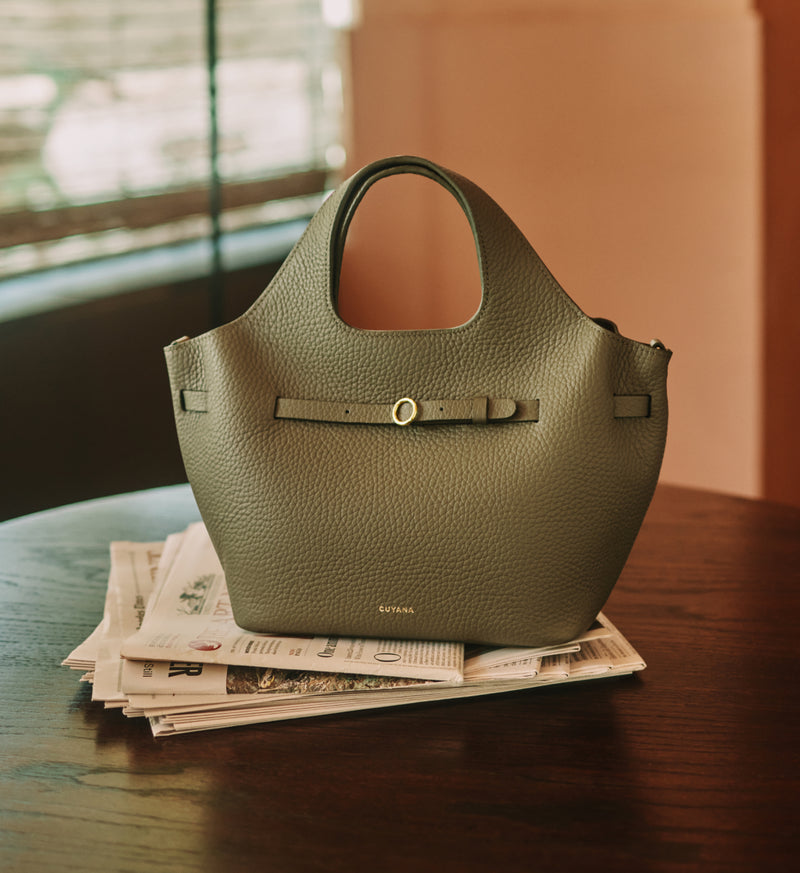 Handbag on a stack of newspapers on a wooden table.