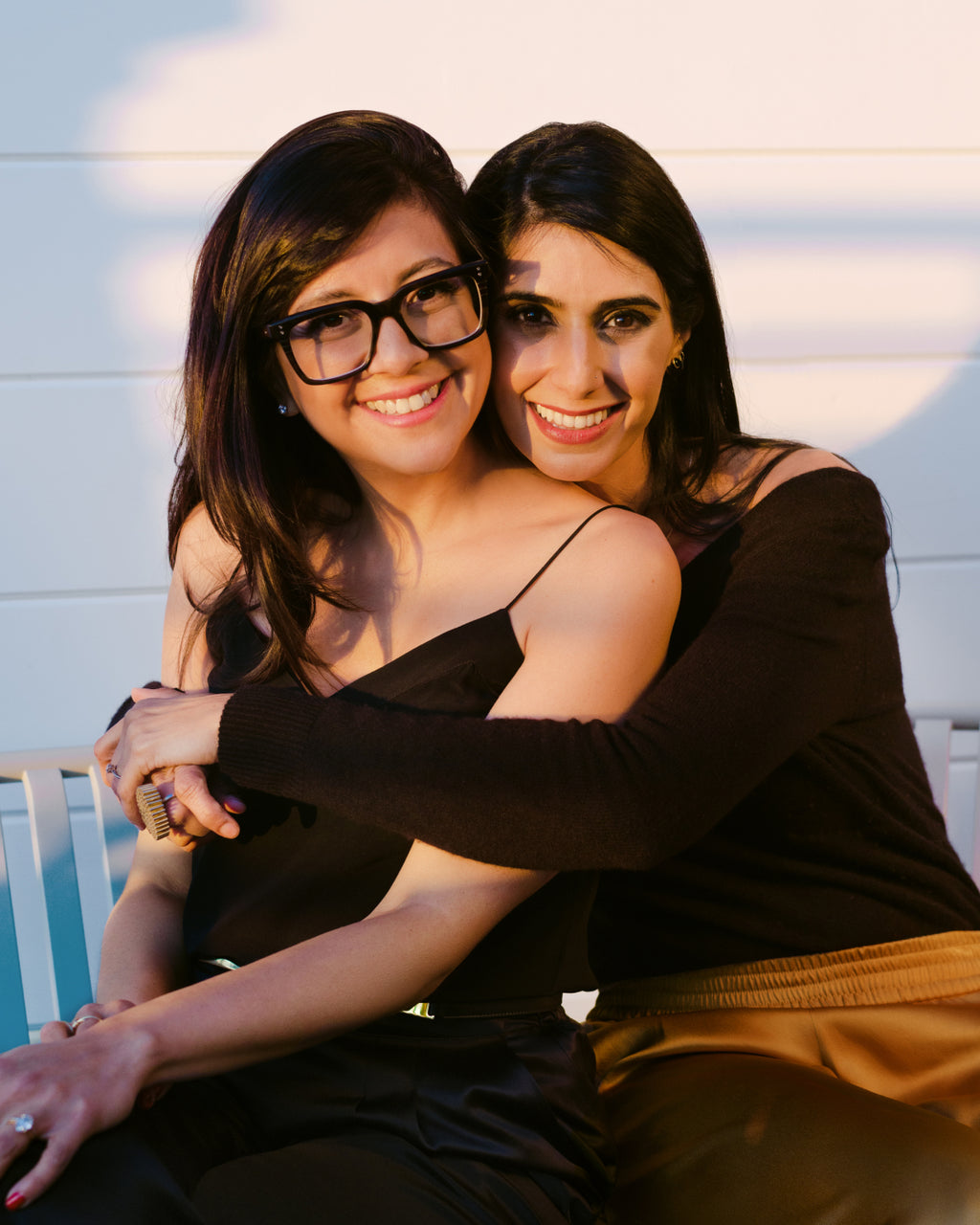 Two people sitting on a bench, one person is hugging the other.