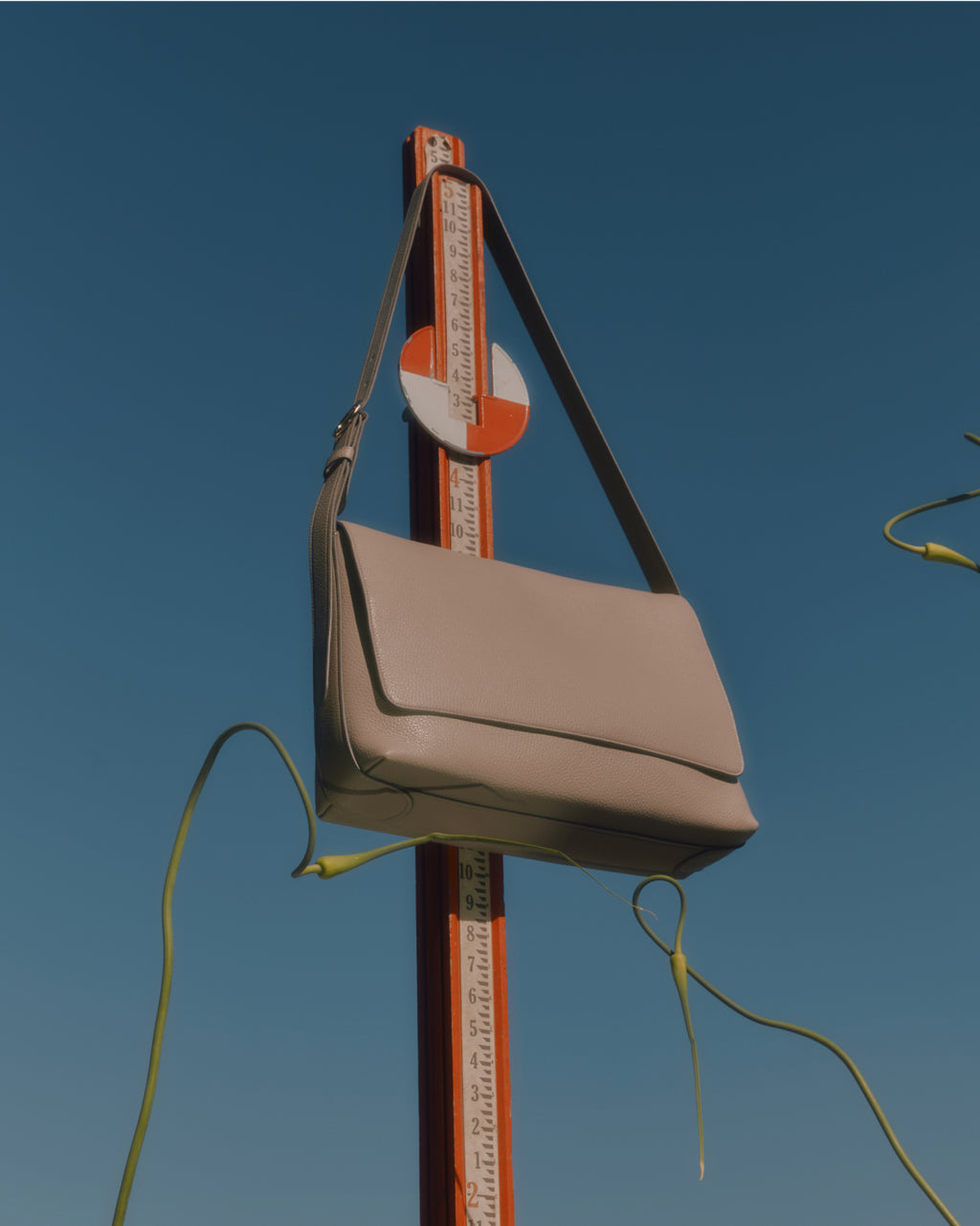 A shoulder bag hanging on a tall measuring stick against a clear sky.