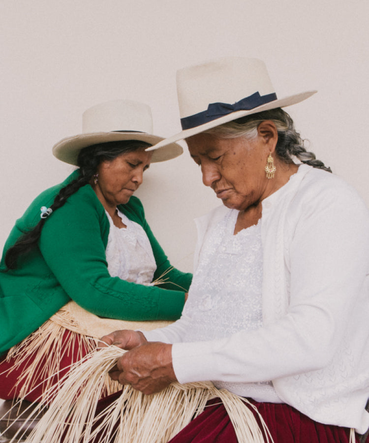 Two women wearing hats weaving straw.