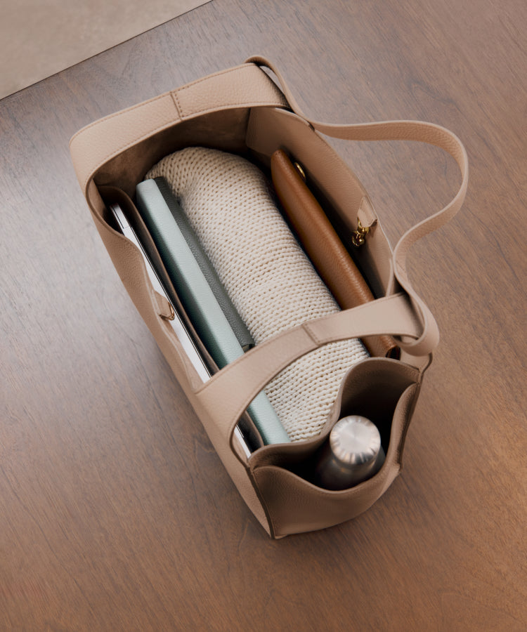 Tote bag containing a notebook, sweater, pen case, and water bottle on a wooden surface