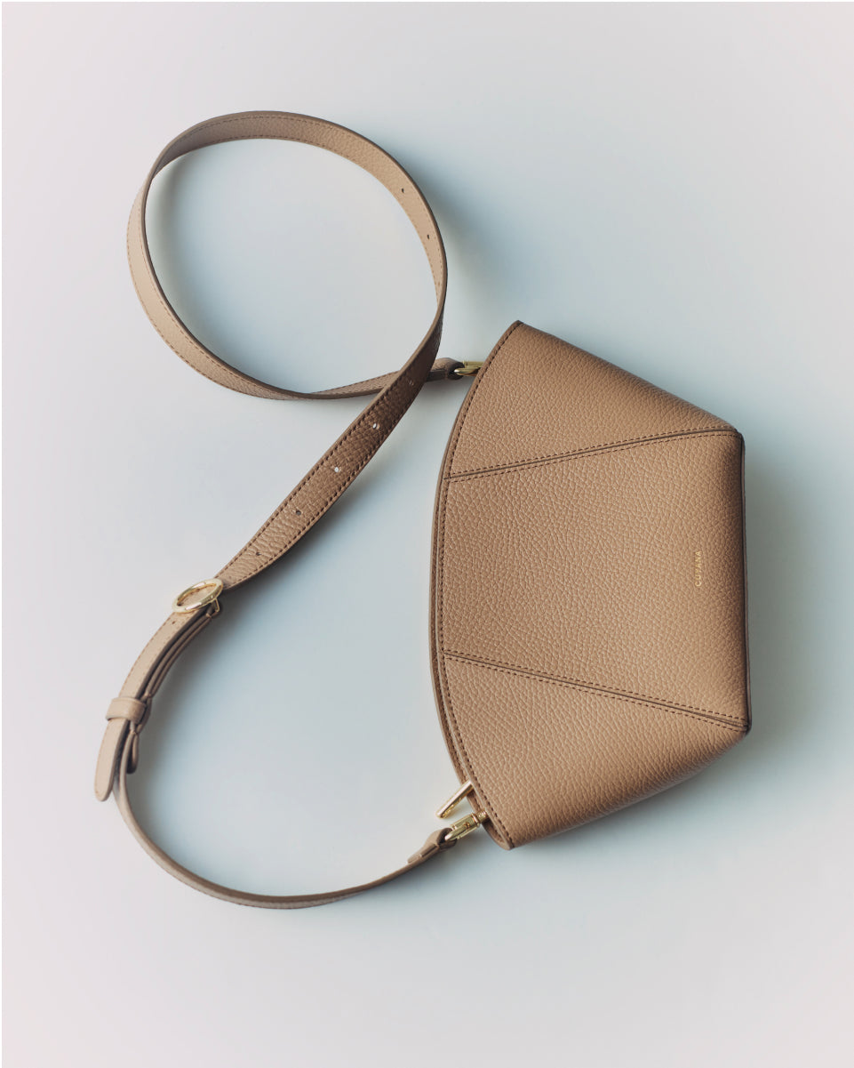 A structured crossbody bag with an adjustable strap on a plain background.