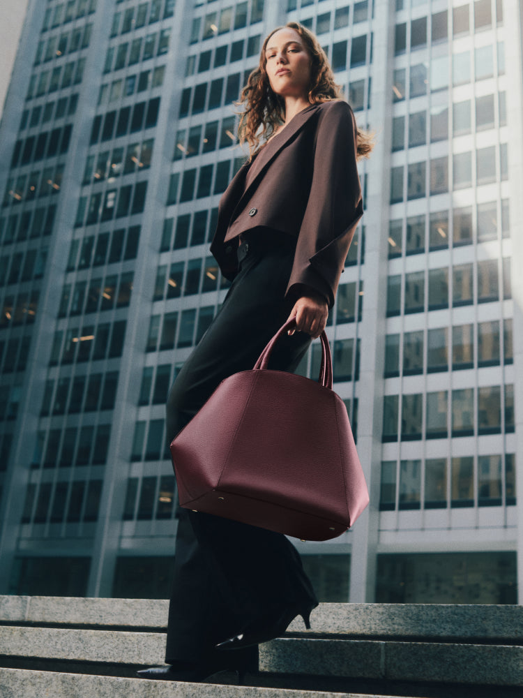 Person holding a large handbag stands in front of a tall office building