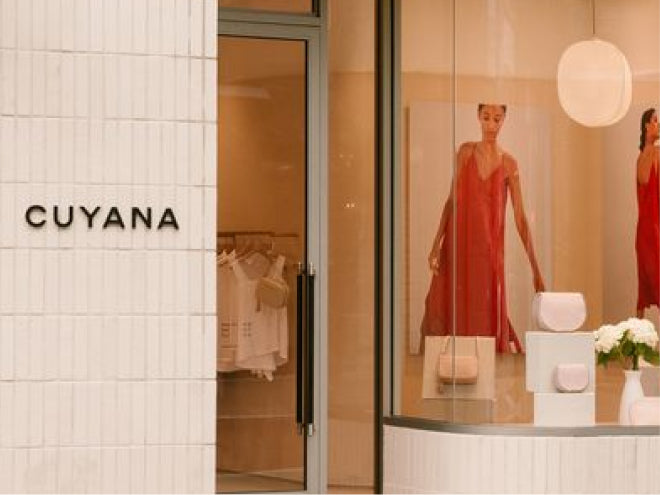 Storefront with mannequins in dresses and bags displayed, signage on the wall.