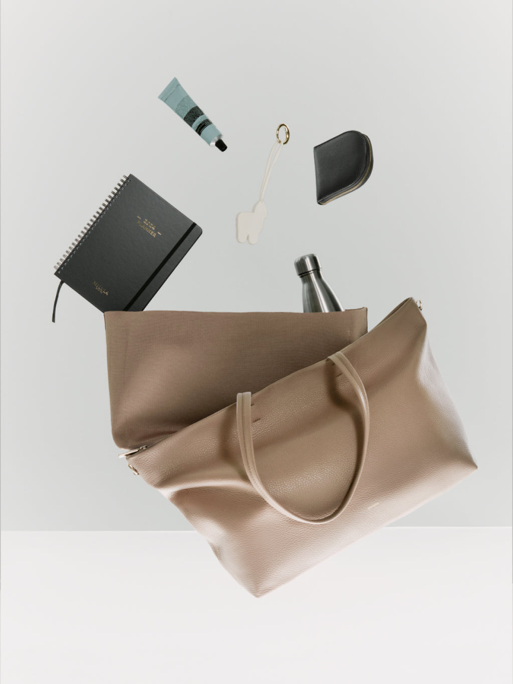 Items floating above a tote bag including a notebook, bottle, and keys.