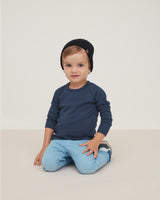 Child sitting on floor wearing a beanie and long-sleeve shirt.