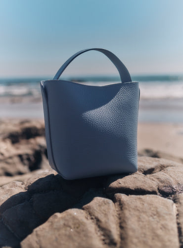 Handbag on a rock by the beach with waves in the background.