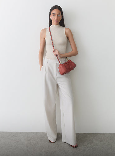 Person wearing sleeveless top and wide pants, holding a small bag with shoulder strap.