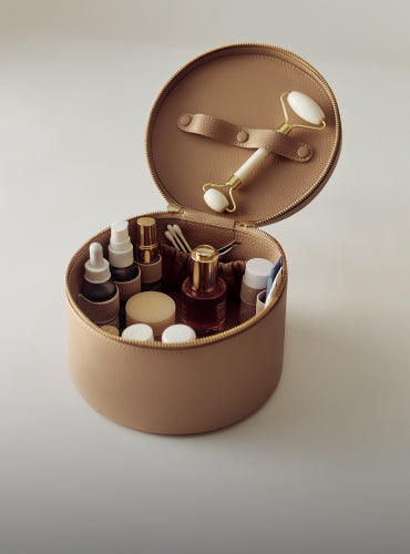 Round cosmetic case with skincare bottles and roller tool.