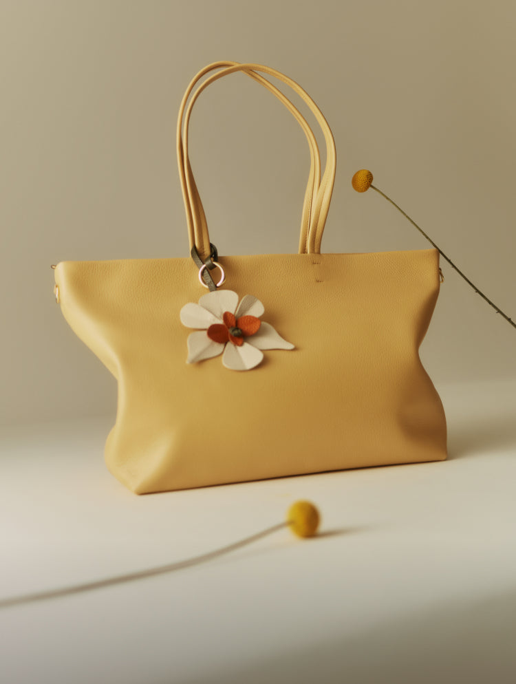Handbag with flower decor beside small round flowers on long stems.