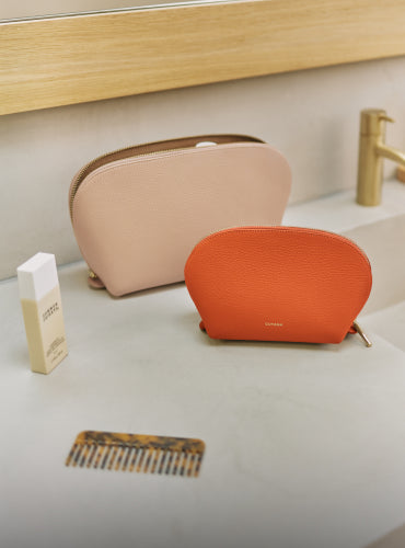 Two cosmetic pouches on a counter with a cream and a comb nearby.