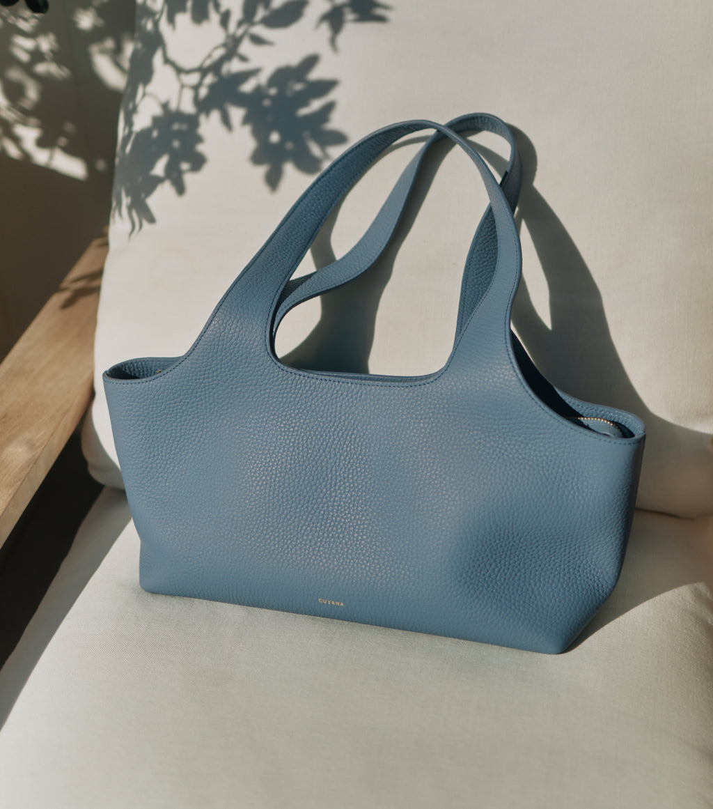Tote bag on a cushioned chair with shadows from nearby leaves.