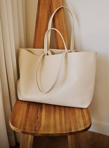Large tote bag on a wooden chair next to a curtain.