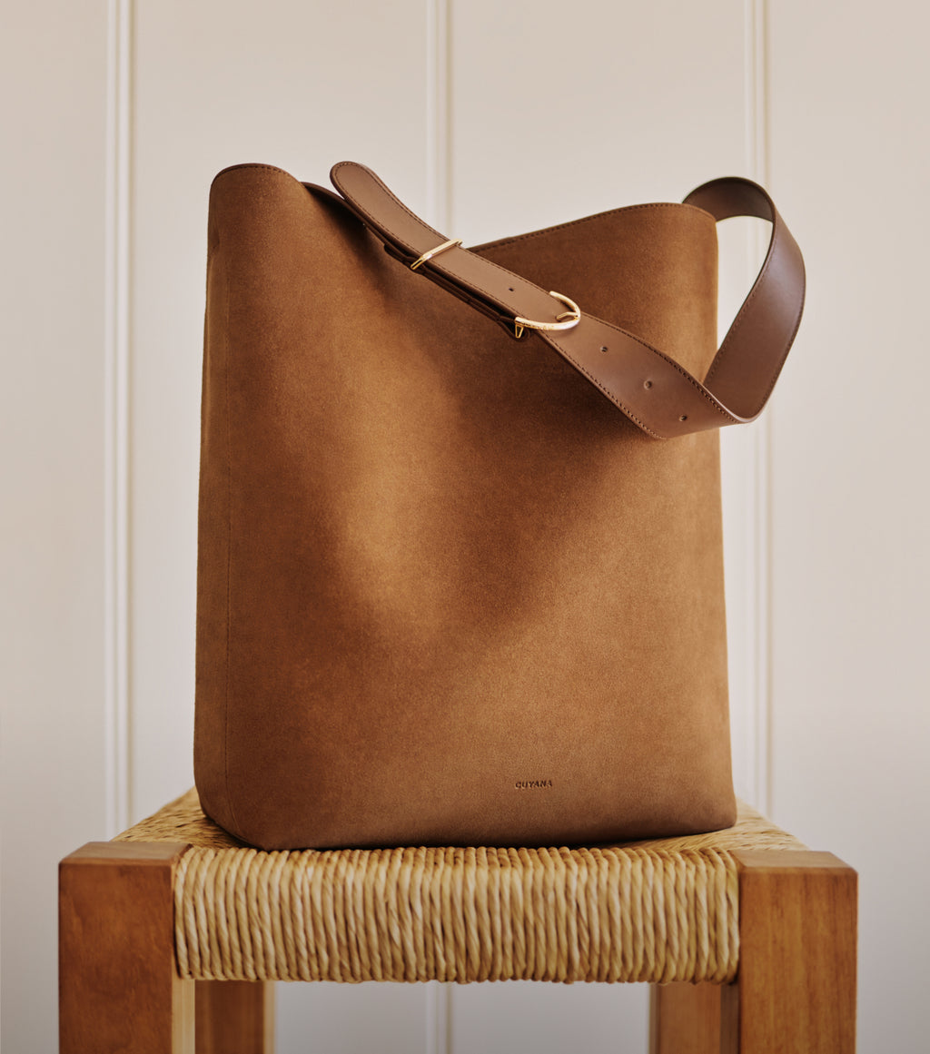 Tall suede purse with single strap on woven chair.