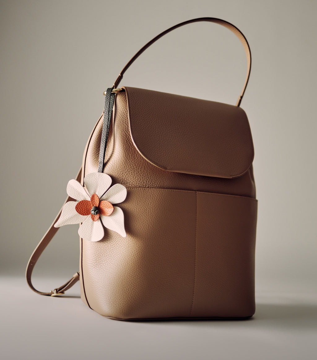 Backpack with a top handle and flower-shaped charm.