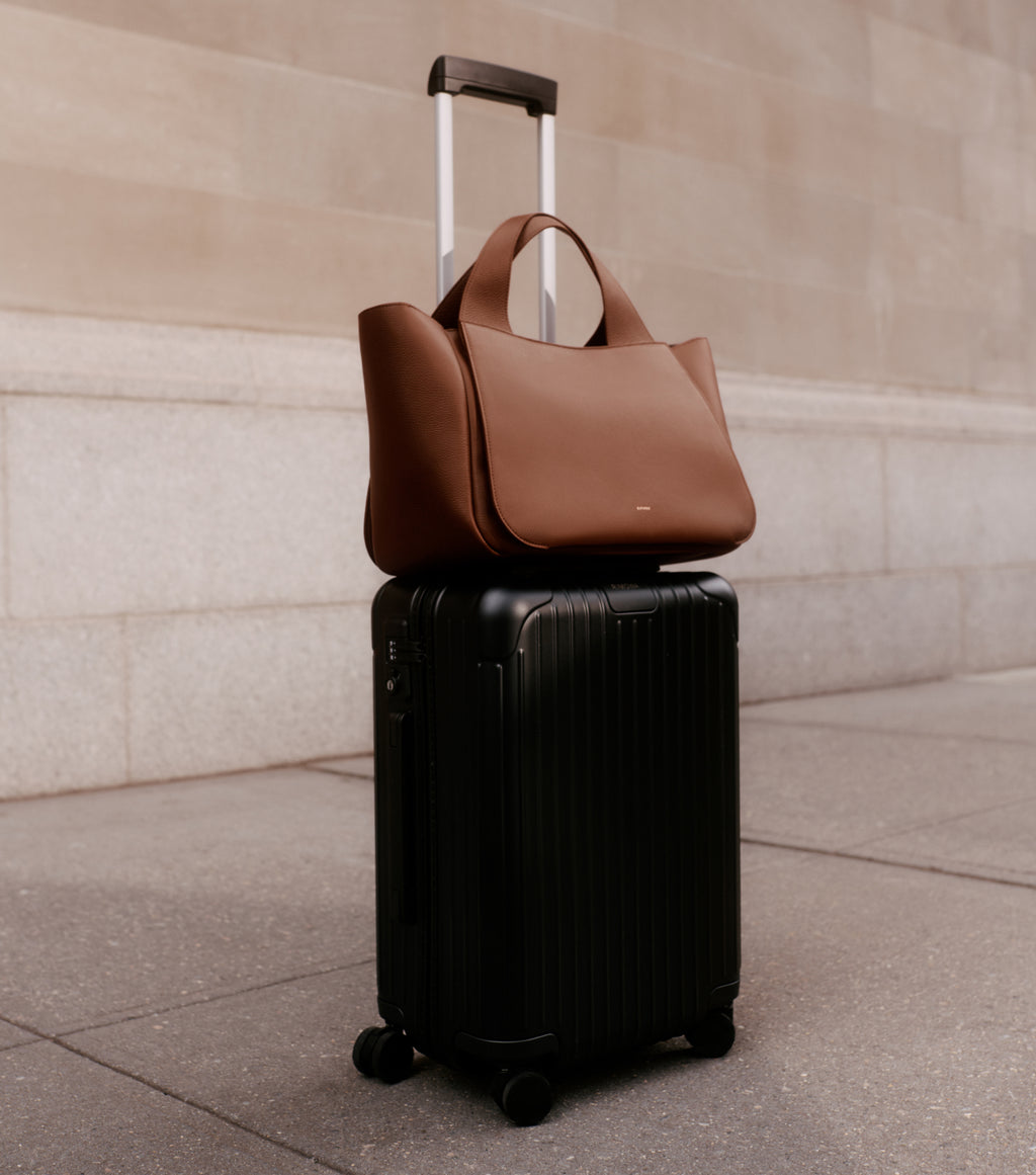 Suitcase with a travel bag on top standing on pavement near a wall.