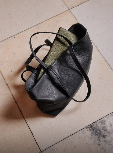 A travel bag with a large strap resting on tiled floor.