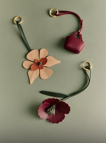 Two floral leather keychains and a mini bag keychain with loop handles on a flat surface.