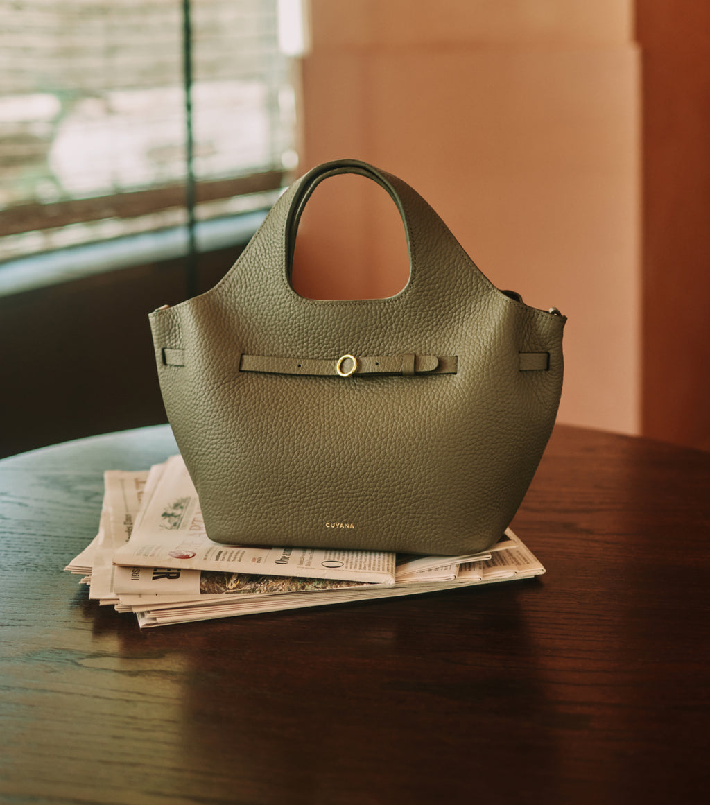 Handbag resting on a stack of newspapers on a table.