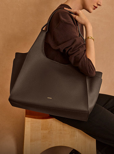 Person sitting on stool holding a large tote bag