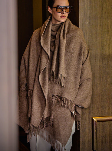 Person wearing a cape and sunglasses, standing indoors near a wall.
