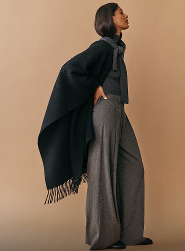 Person wearing a cape and loose-fitting pants standing in profile.