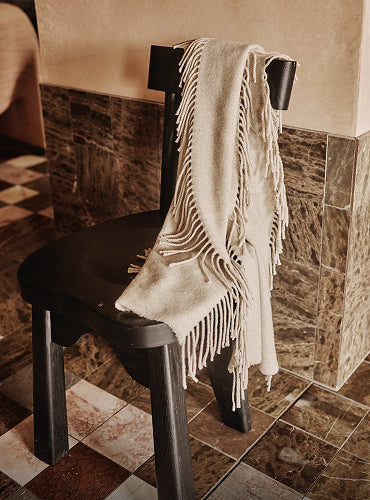 Fringed shawl draped over back of a chair in room with tiled floor.