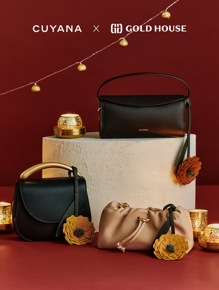 Three handbags with floral accents displayed on a round pedestal with candle decor.