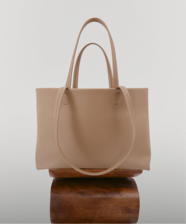 A tote bag with two handles displayed on a wooden stand.