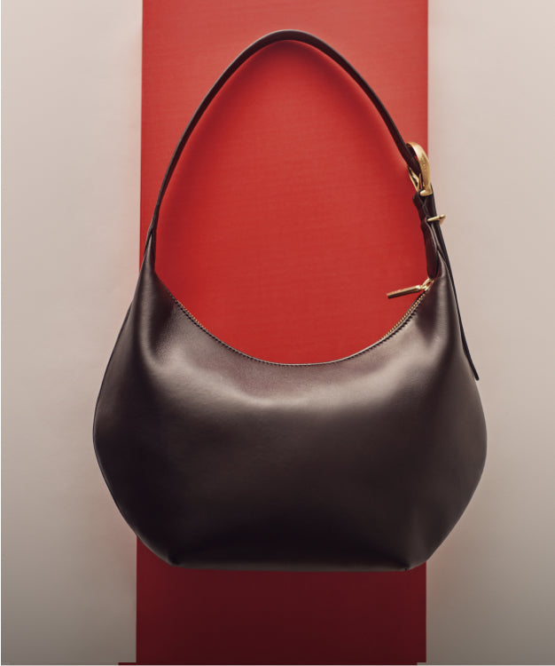 Handbag with curved handle against vertical red and white backdrop.