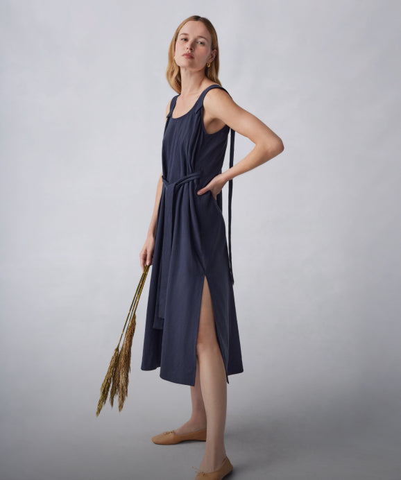 Linked Image: Directs to Dresses shop page (cuyana.com/collections/dresses). Image description: Model wearing the Cuyana Linen Gathered Back Dress in Navy. 