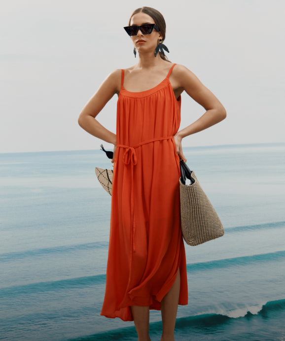 Woman in long dress with a large tote bag near a body of water.