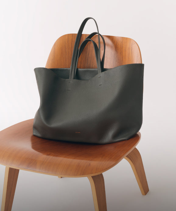 Dark green leather tote sits on wooden chair. Linked image.