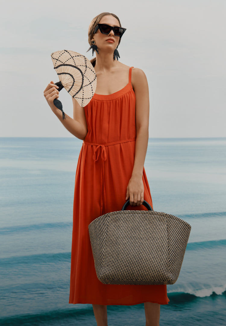 Person standing by the sea holding a fan and a large bag