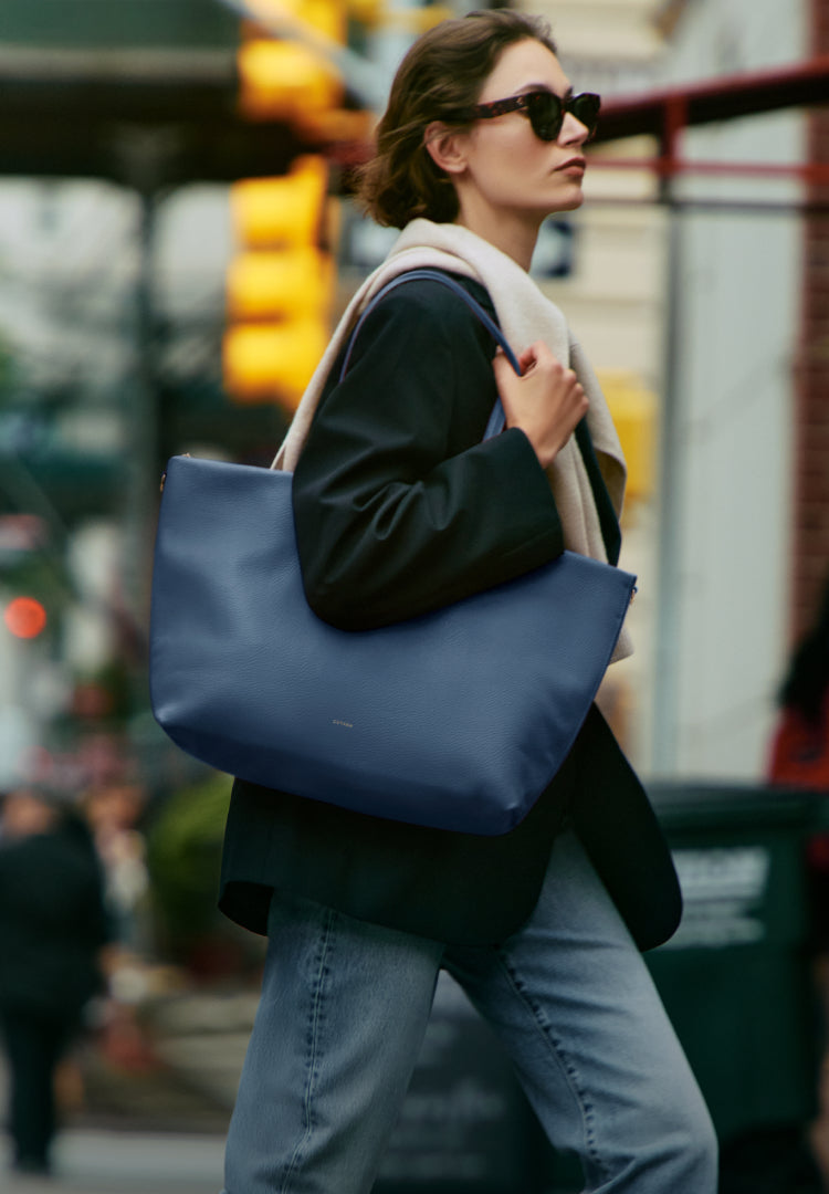 Person walking in city carrying large tote bag over shoulder.