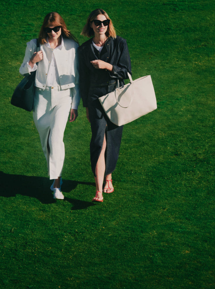 Two people walking on grass, each holding a large bag and wearing sunglasses.