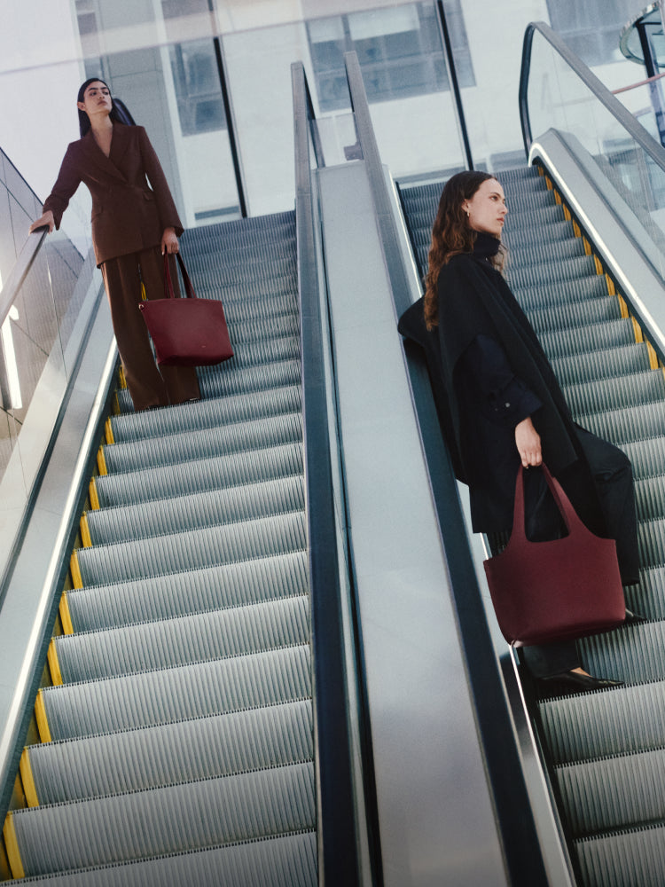 Two people on opposite escalators holding large bags.