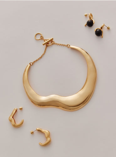 Curved necklace with matching earrings and black stud earrings displayed on a surface.