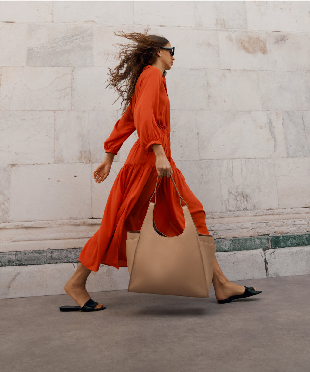 Linked Image: Directs to Summer Collection preview. Image Description: Model wearing Cuyana Tencel Verano Dress in color Tangerine and carrying the Cuyana Double Loop Satchel in color Cappuccino.