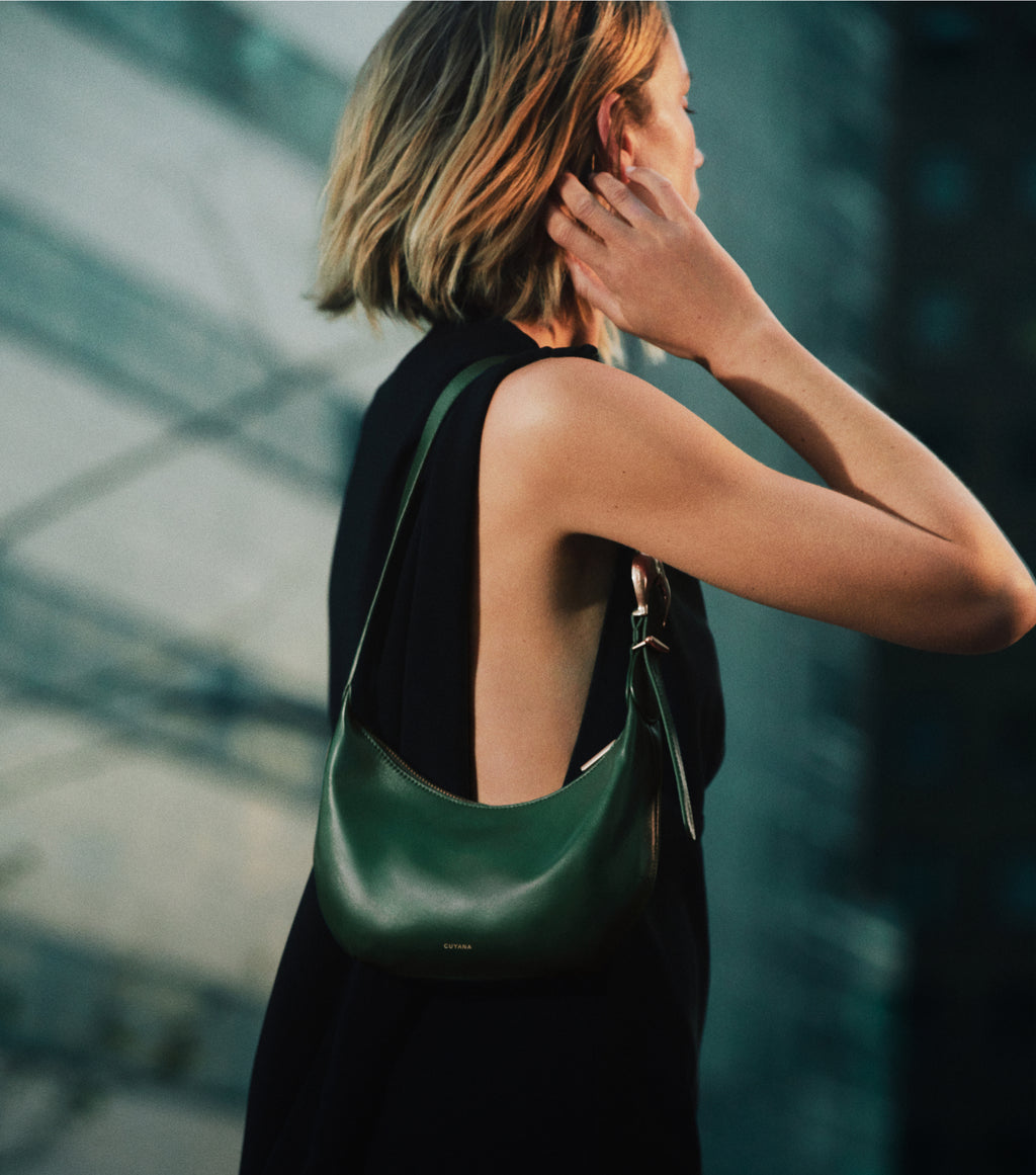 Person holds shoulder bag with arm raised, standing outdoors.