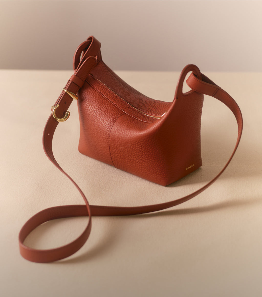 A small leather shoulder bag with a long strap on a flat surface.