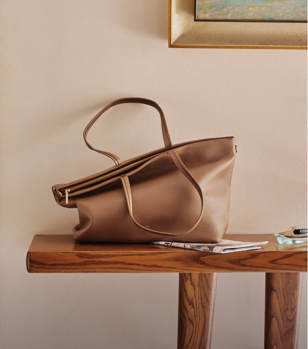 Large soft tote with two handles and a zipper sits on top of a newspaper on a wooden table. 