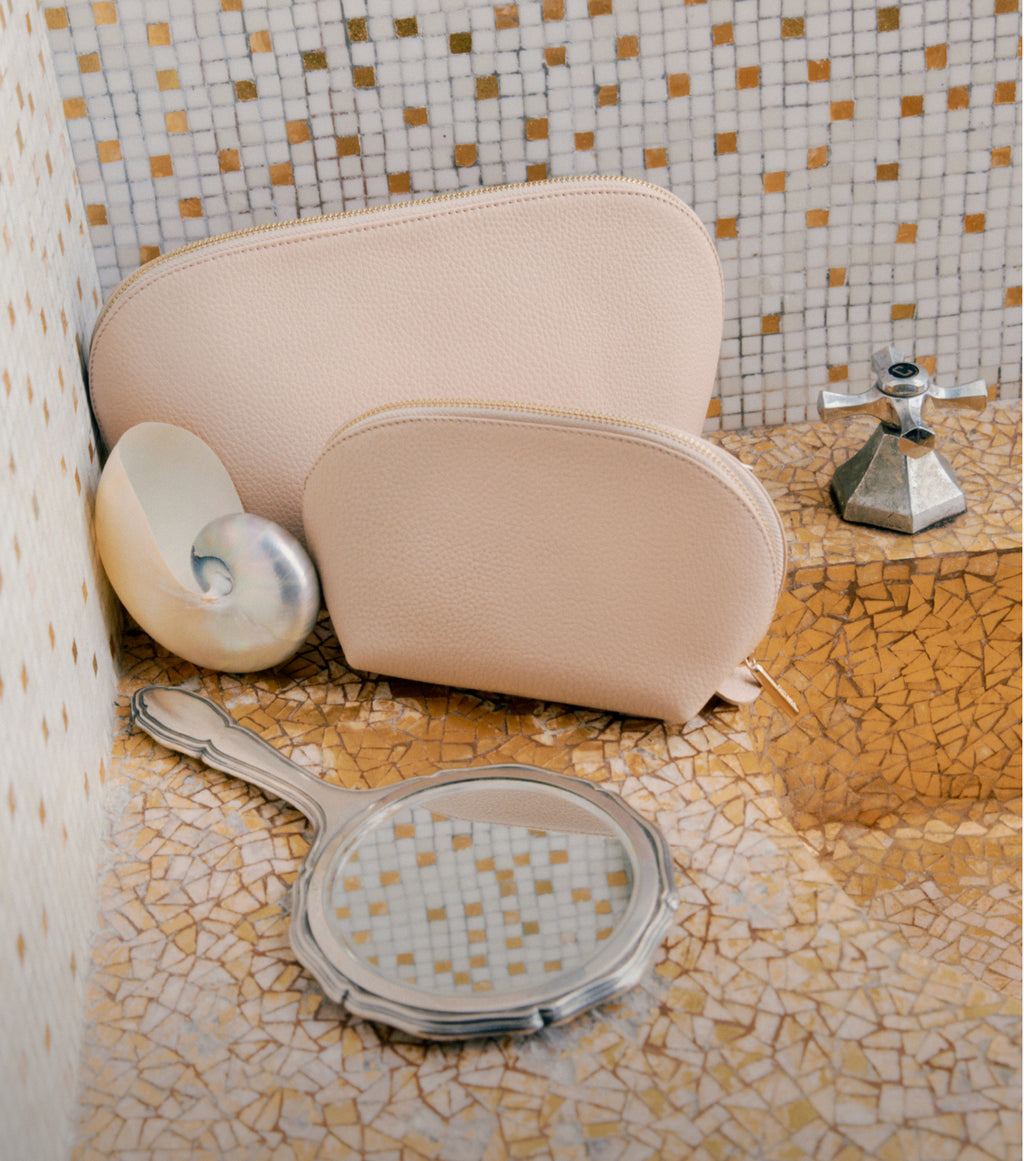 Leather pouches, a handheld mirror and a sea seashell on a tiled surface. 