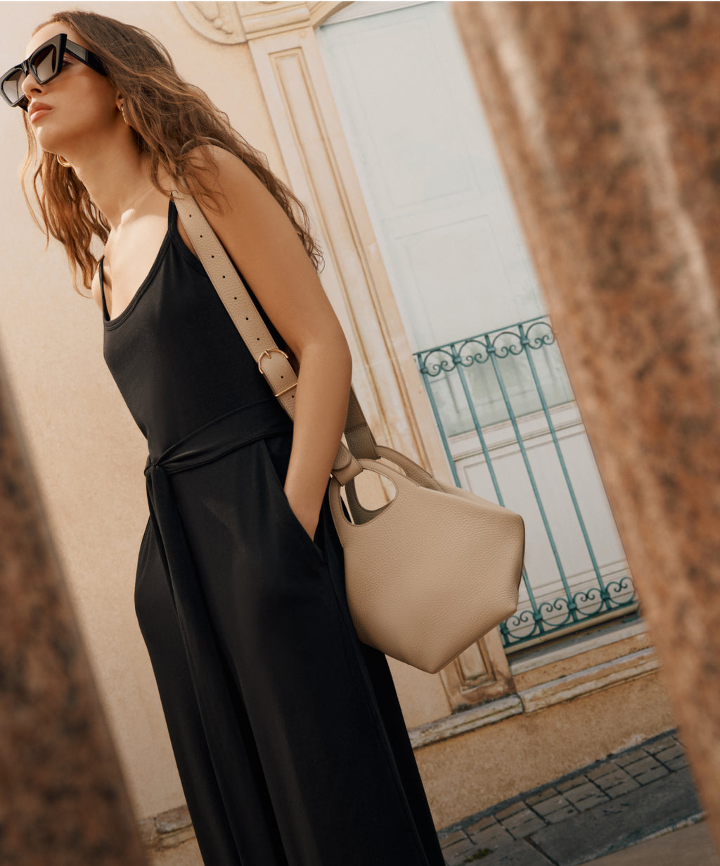 Model in black carries beige purse over shoulder. Linked Image