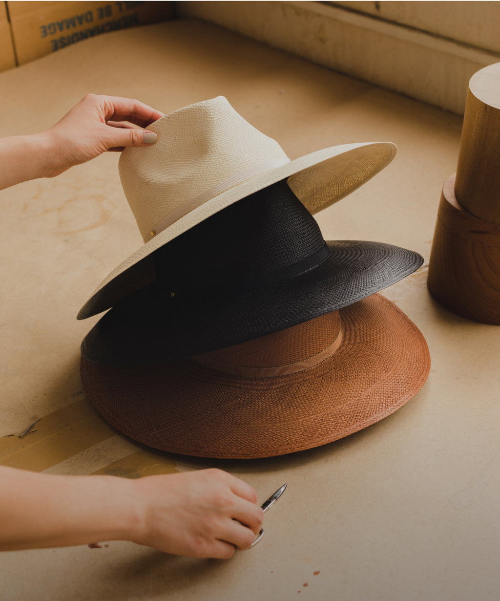 Three hats stacked, with a hand arranging the top one in a light room.