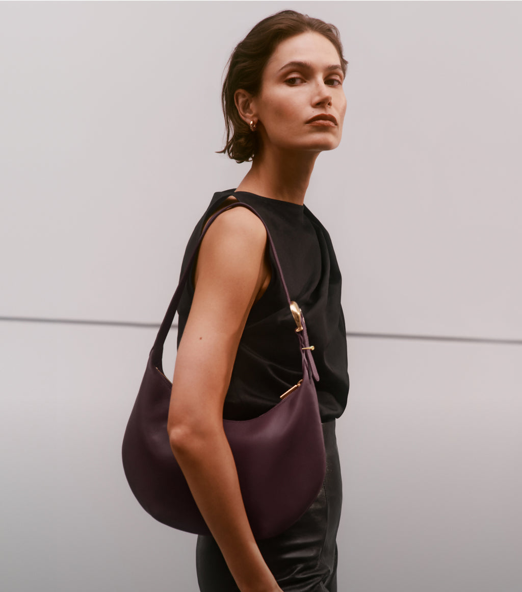 Person with a shoulder bag poses against a plain background.