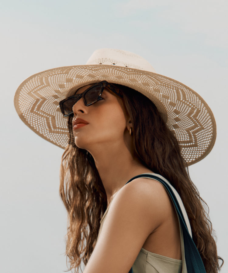Woman wearing a wide-brimmed hat and sunglasses, looking upwards.