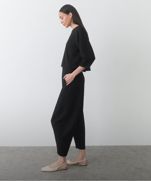 Person in matching top and pants standing sideways in a neutral room.