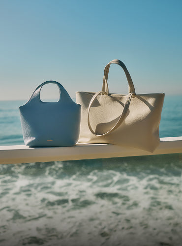 Two tote bags on a ledge with ocean background.